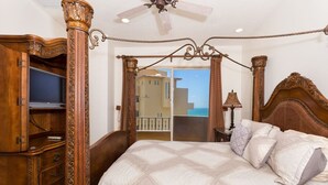 Un dormitorio con una cama grande, muebles de madera y vista al mar por una puerta abierta.