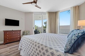 Un dormitorio con cama, cómoda, televisión y balcón con cortinas.