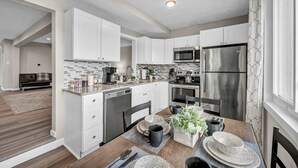 A modern kitchen with white cabinets, stainless steel appliances, and a dining area with a wooden table and chairs.
