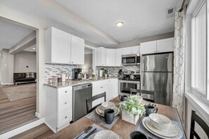 A modern kitchen with white cabinets, stainless steel appliances, and a dining area with a wooden table and chairs.