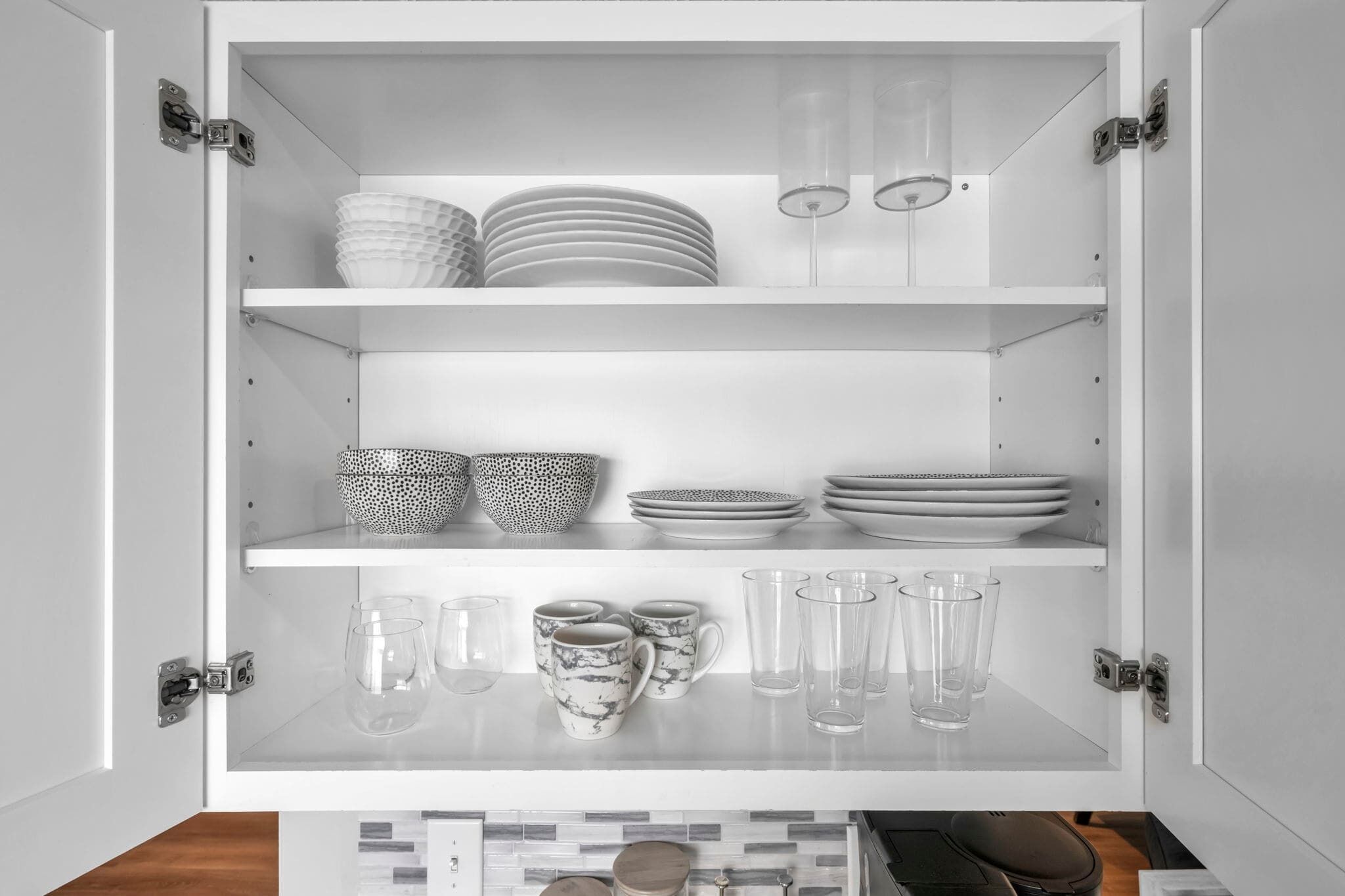 Un mueble blanco con estantes que contiene platos, tazones, vasos y una cafetera.