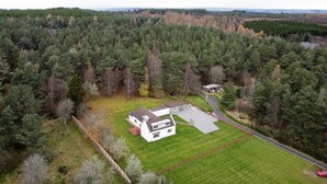 An aerial view of a two-story house with a large lawn, surrounded by dense forest.