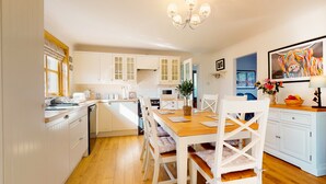 A modern kitchen with white cabinets, a wooden dining table, and a chandelier.