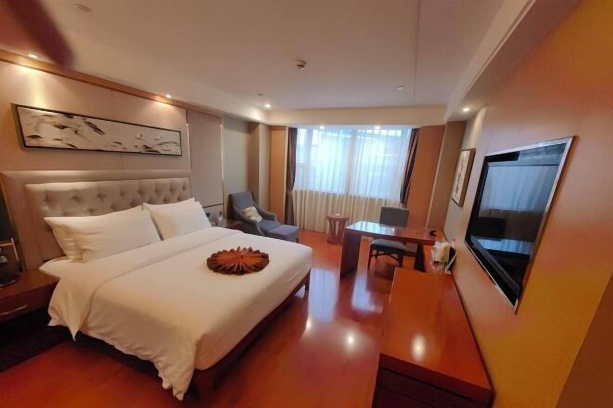 Une chambre d’hôtel avec un grand lit, un bureau, une chaise, une télévision et une fenêtre avec des rideaux.
