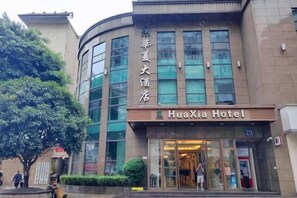 Ein Hotel mit einer geschwungenen Fassade, großen Fenstern und einem Schild mit der Aufschrift 'HuaXia Hotel'.