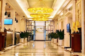A hotel lobby with a marble floor, a reception desk, potted plants, and a large chandelier. - Dazhou Huaxia Grand Hotel (Dazhou Central Plaza) (Dazhou)