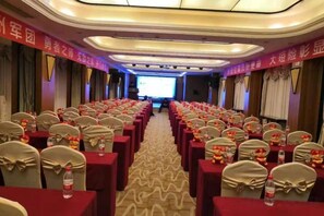 Un salón de conferencias con filas de mesas y sillas, un escenario al frente y pancartas en las paredes.