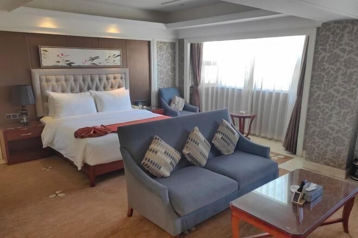 A hotel room with a bed, a sofa, a small table, and a window with curtains.