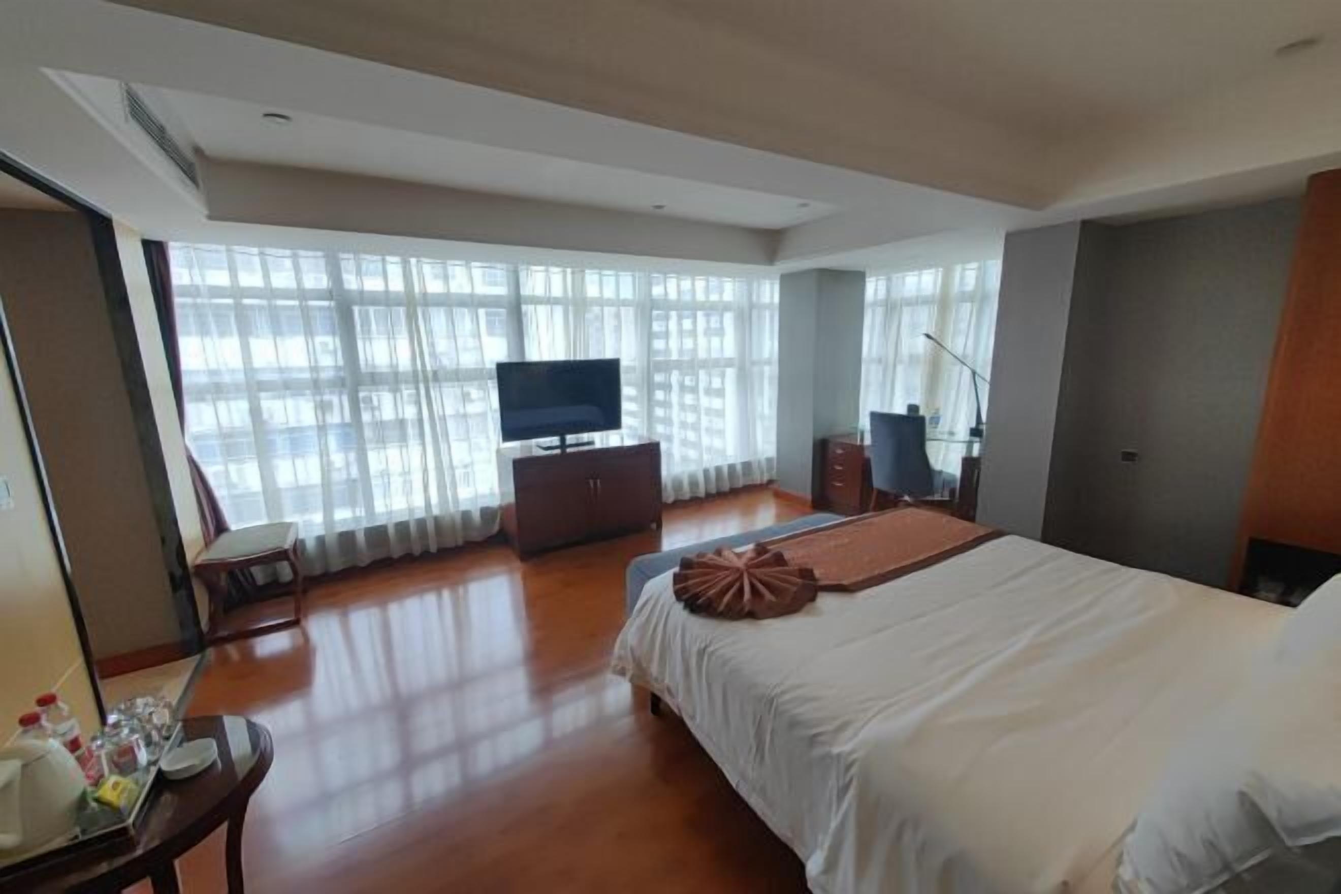 A hotel room with a large bed, a TV, a dresser, and a desk with a chair.