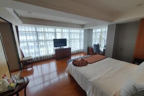 A hotel room with a large bed, a TV, a dresser, and a desk with a chair. - Huaxia Hotel (Dazhou)