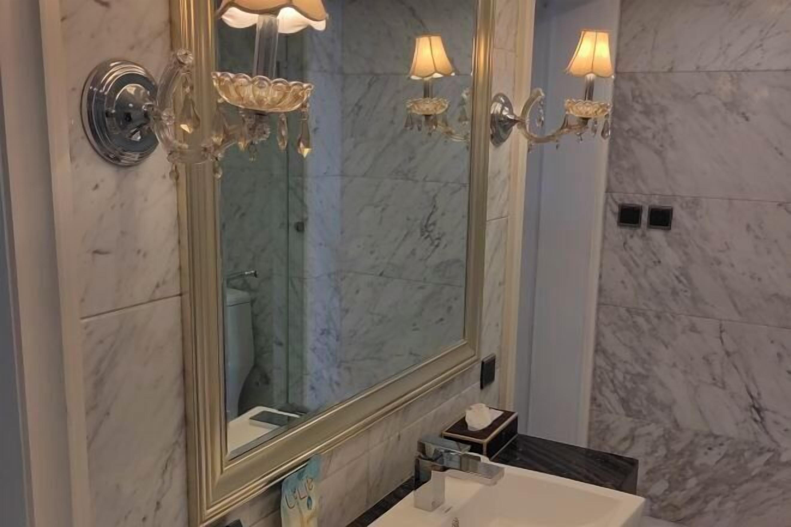 Un baño con un espejo grande, paredes de mármol e iluminación empotrada.