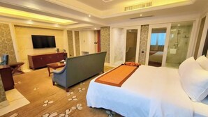 A hotel room with a bed, a desk, a chair, a TV, and a bathroom with a glass door. - Huaxia Hotel (Dazhou)