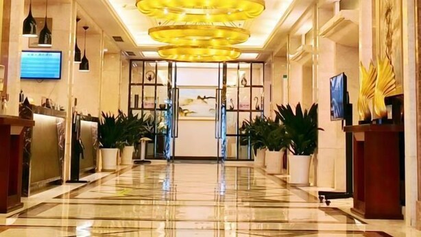 A hotel lobby with a marble floor, a reception desk, potted plants, and a large chandelier. - Huaxia Hotel (Dazhou)
