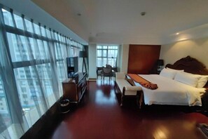 A hotel room with a large bed, a desk, a chair, and a view of the city through large windows. - Huaxia Hotel (Dazhou)