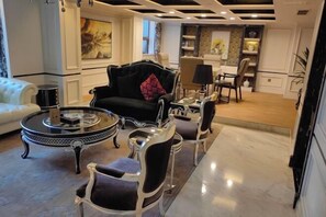 A modern living room with a black sofa, white armchairs, and a glass coffee table. There is a dining area with a table and chairs in the background. - Huaxia Hotel (Dazhou)