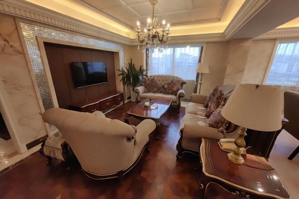 A spacious living room with a large flat-screen TV, a chandelier, and a sofa set.