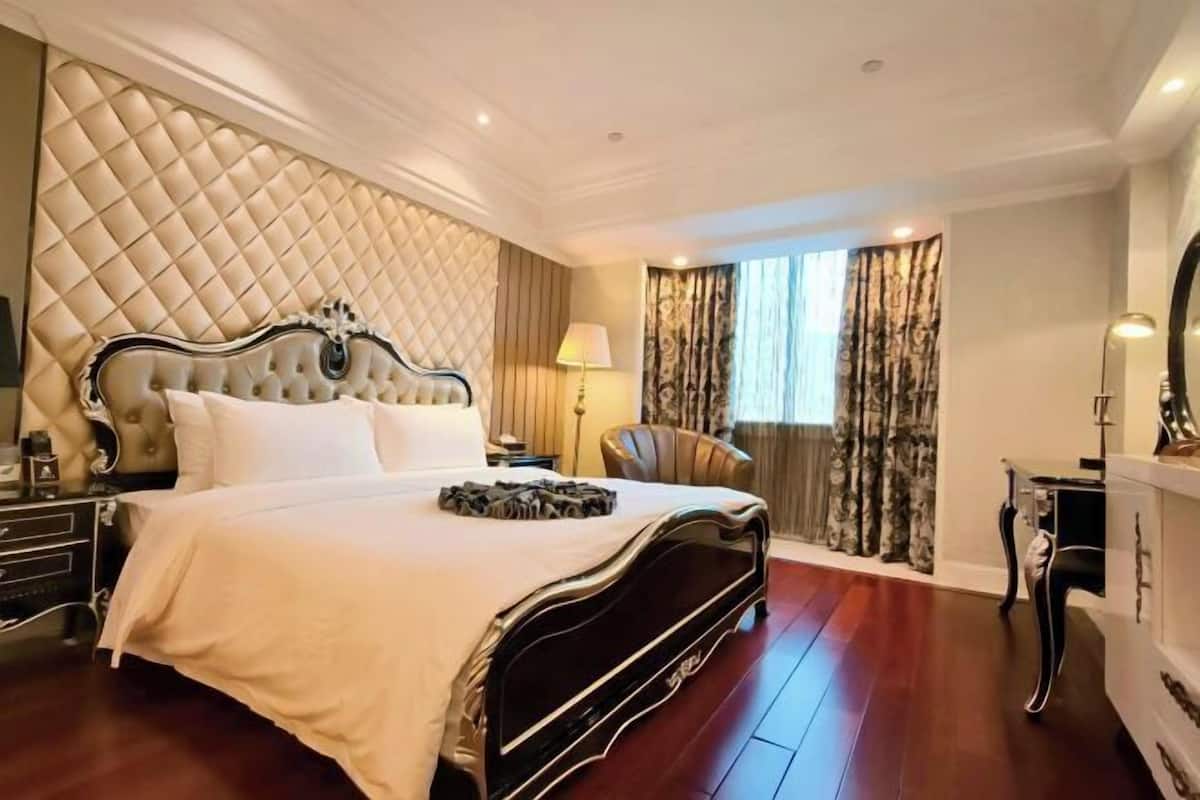 Une chambre spacieuse avec un grand lit, une tête de lit capitonnée, une table de chevet, une chaise, une commode et un miroir.