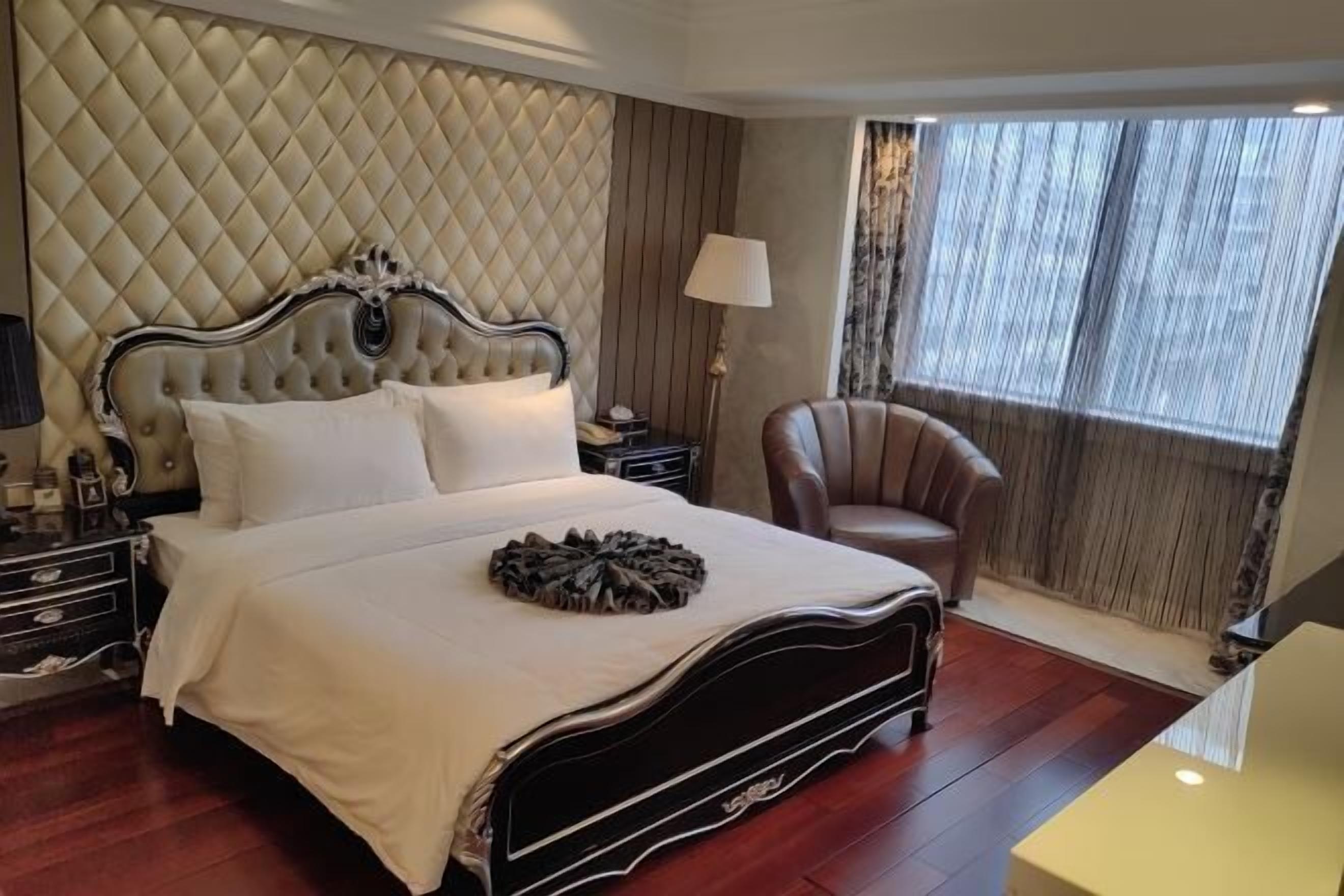 A hotel room with a large bed, a chair, a nightstand, and a window with curtains.
