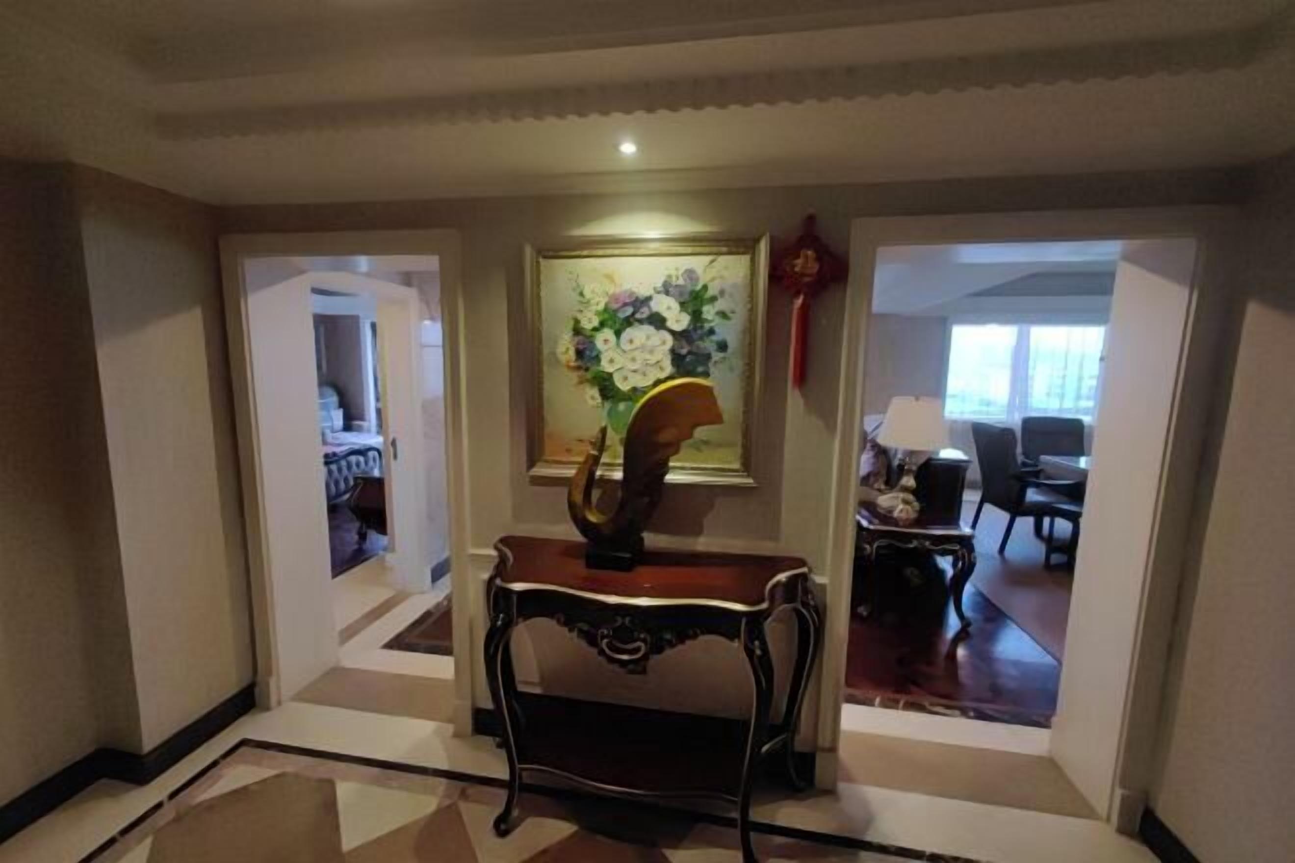 A hallway with a wooden console table, a framed floral painting, and a red decorative item on the wall.
