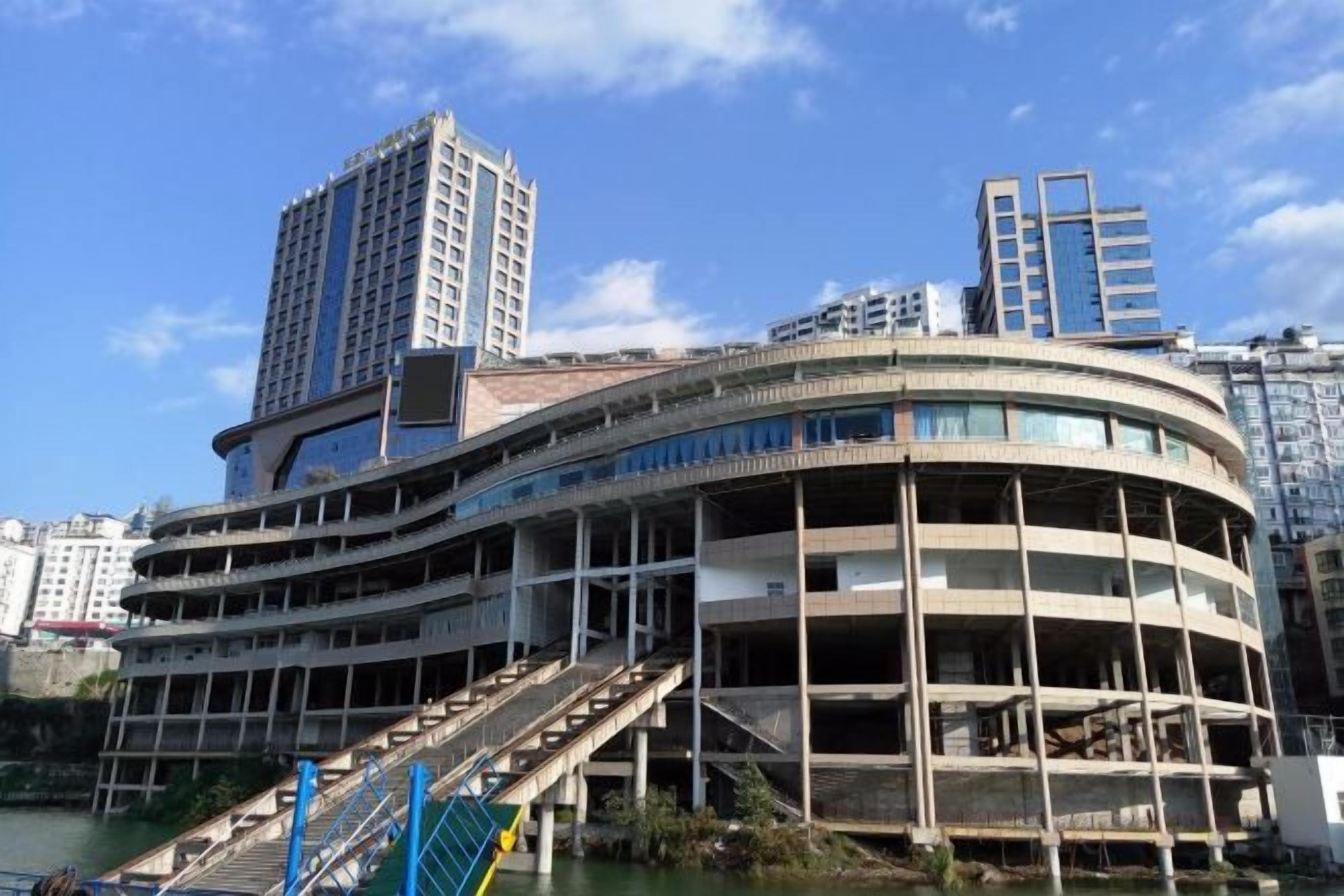 Un edificio de varios pisos con fachada curva, una escalera que conduce a los niveles superiores y un río en primer plano.