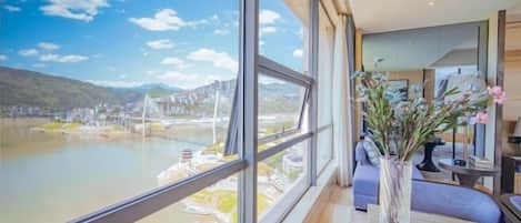 A modern room with large windows overlooking a river and a bridge, a vase with flowers, and a neatly arranged table.