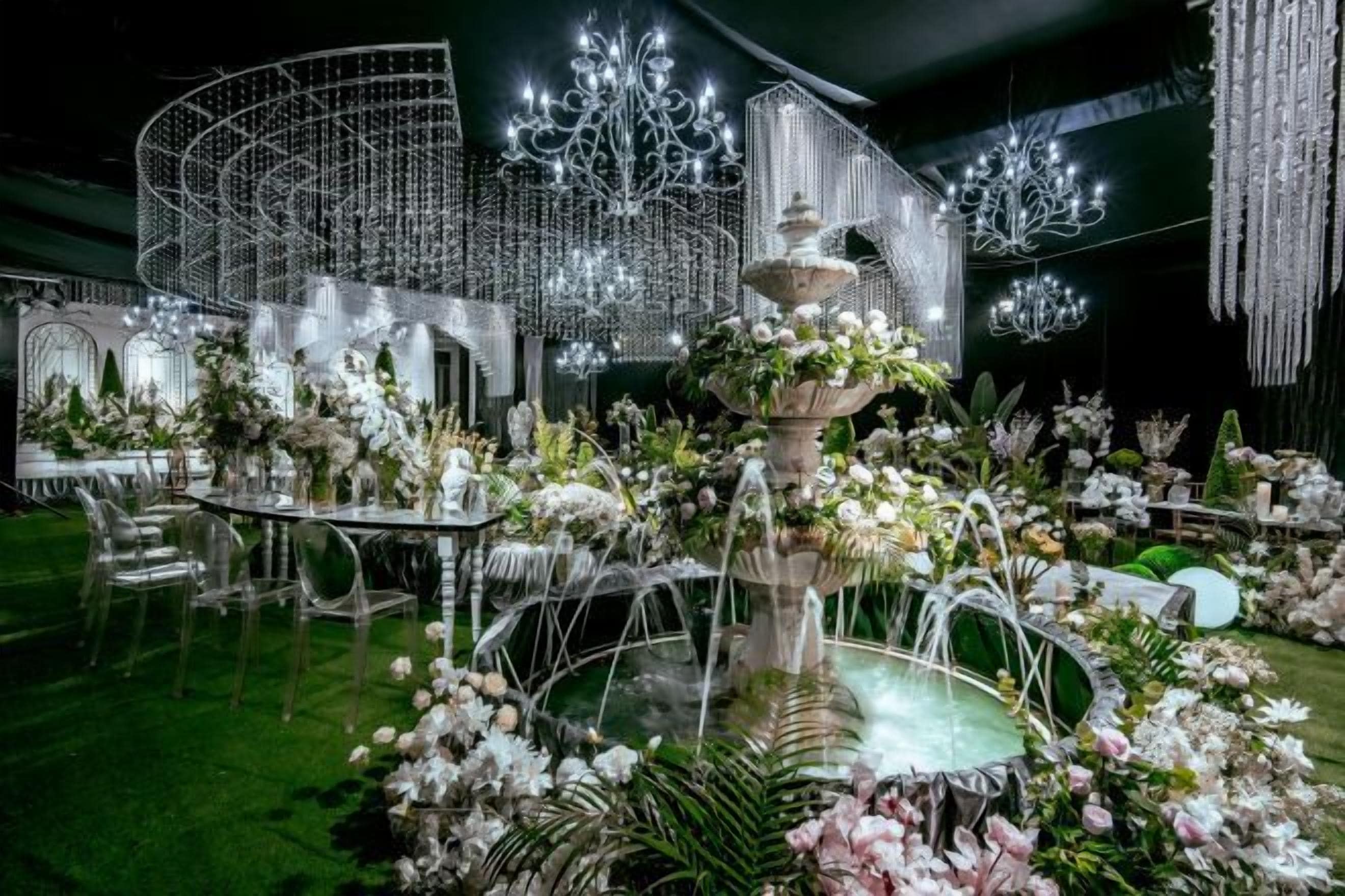 An outdoor event space with tables, chairs, and a central fountain surrounded by floral arrangements.