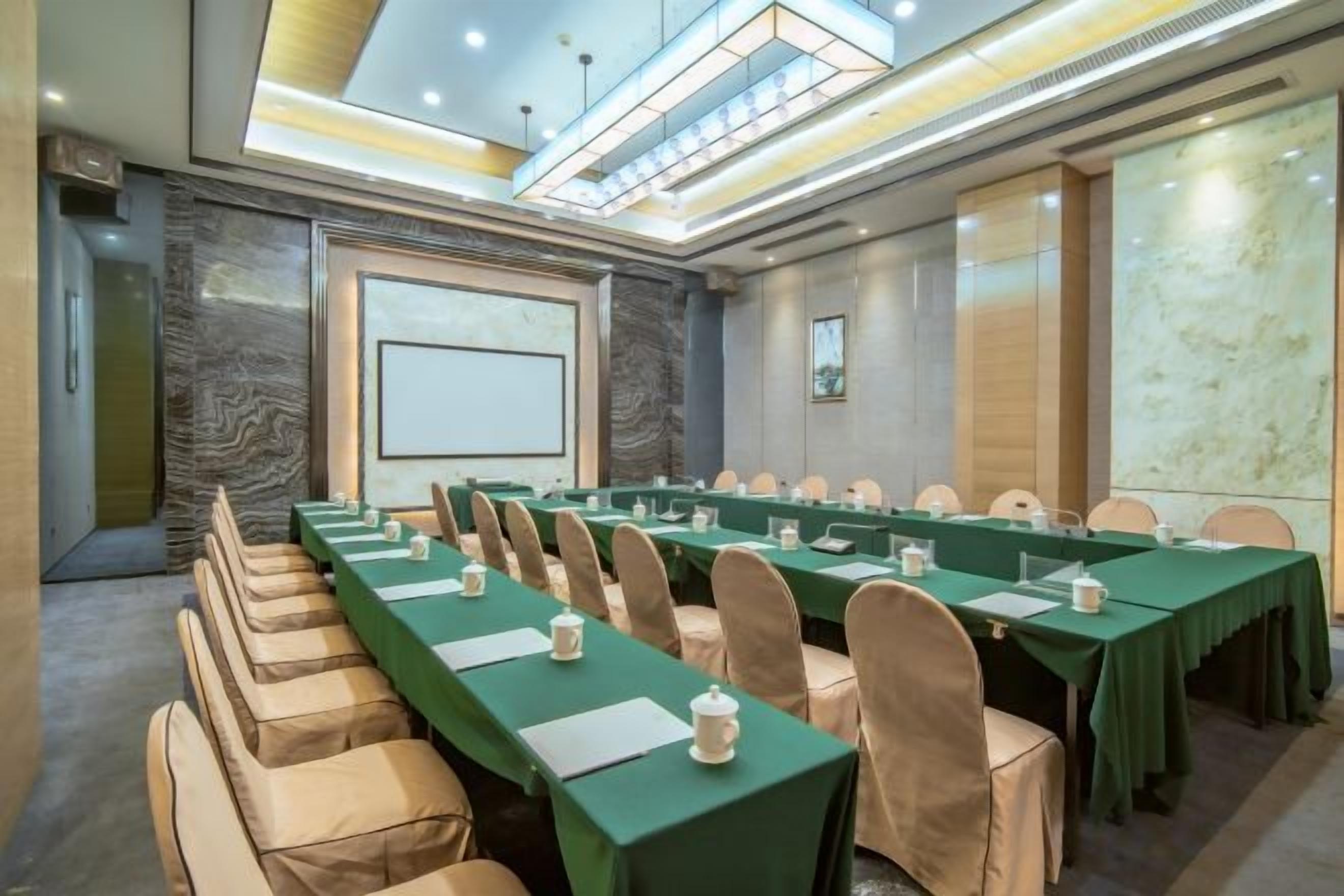 A conference room with long tables, chairs, and a projector screen.