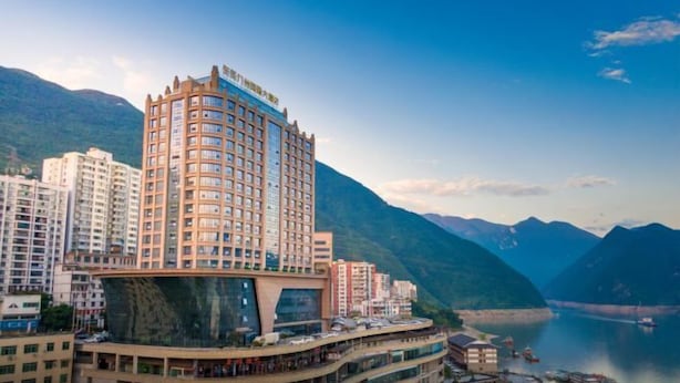 Un hôtel à plusieurs étages, doté d’un design moderne, situé près d’un plan d’eau et entouré de montagnes.
