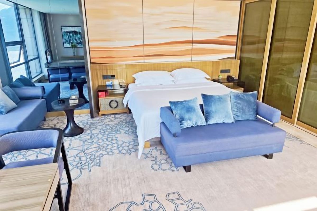 Ein modernes Hotelzimmer mit einem Bett, einer Couch, einem kleinen Tisch und einem großen Fenster.