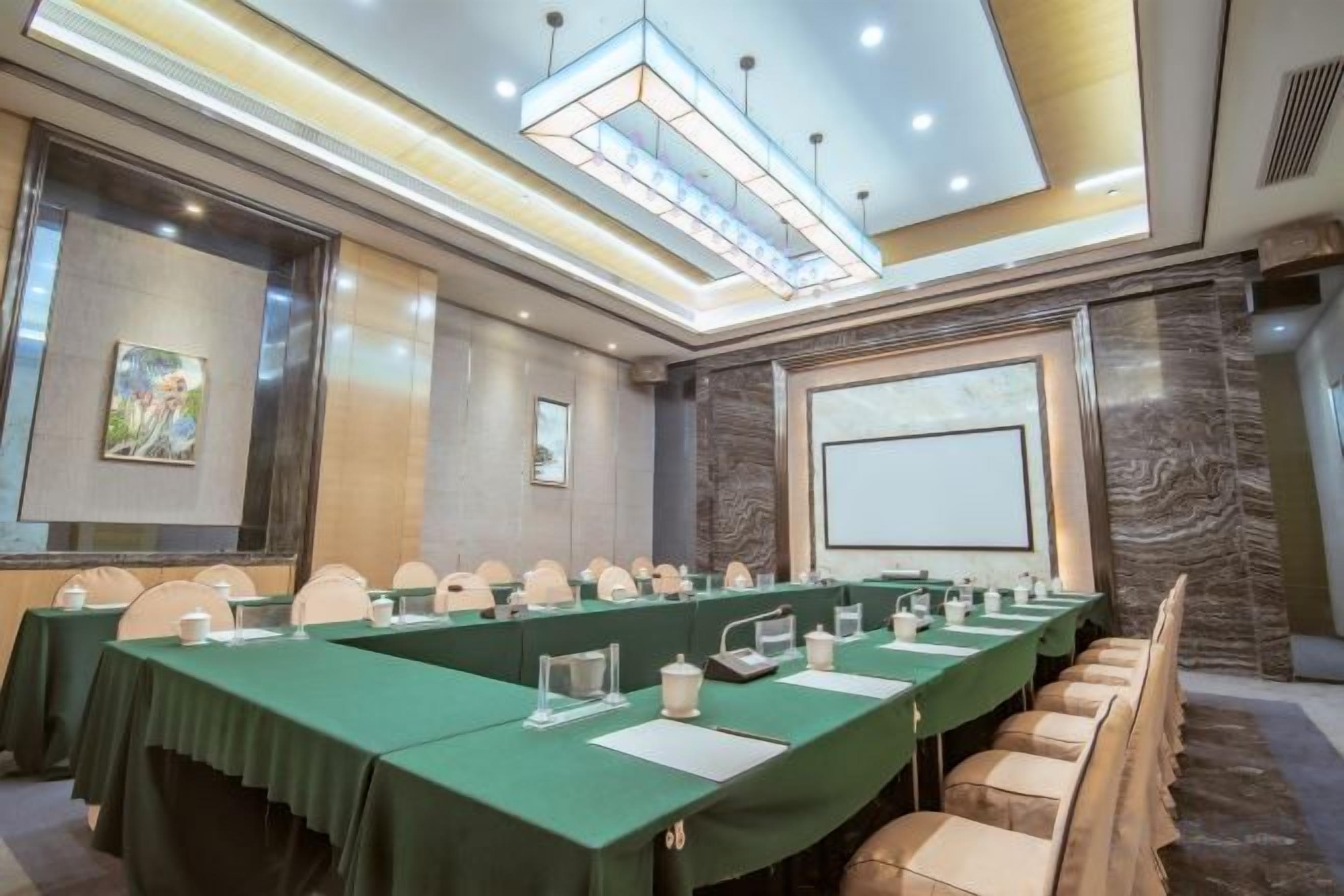A conference room with long tables, chairs, and a projector screen.