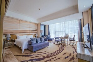 Ett modernt hotellrum med en säng, soffa, skrivbord och stora fönster.