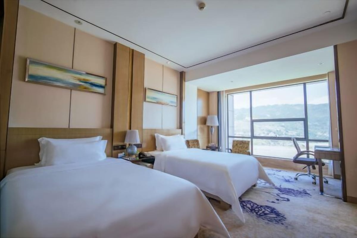 Habitación de hotel con dos camas, un ventanal grande y vistas a las montañas.