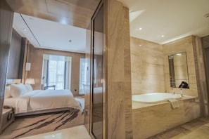 Una habitación de hotel moderna con una cama grande, baño separado con bañera y un espejo amplio.