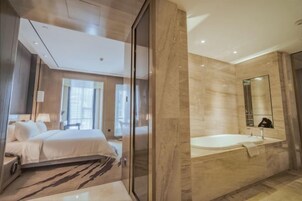 Una habitación de hotel moderna con una cama grande, baño separado con bañera y un espejo amplio.
