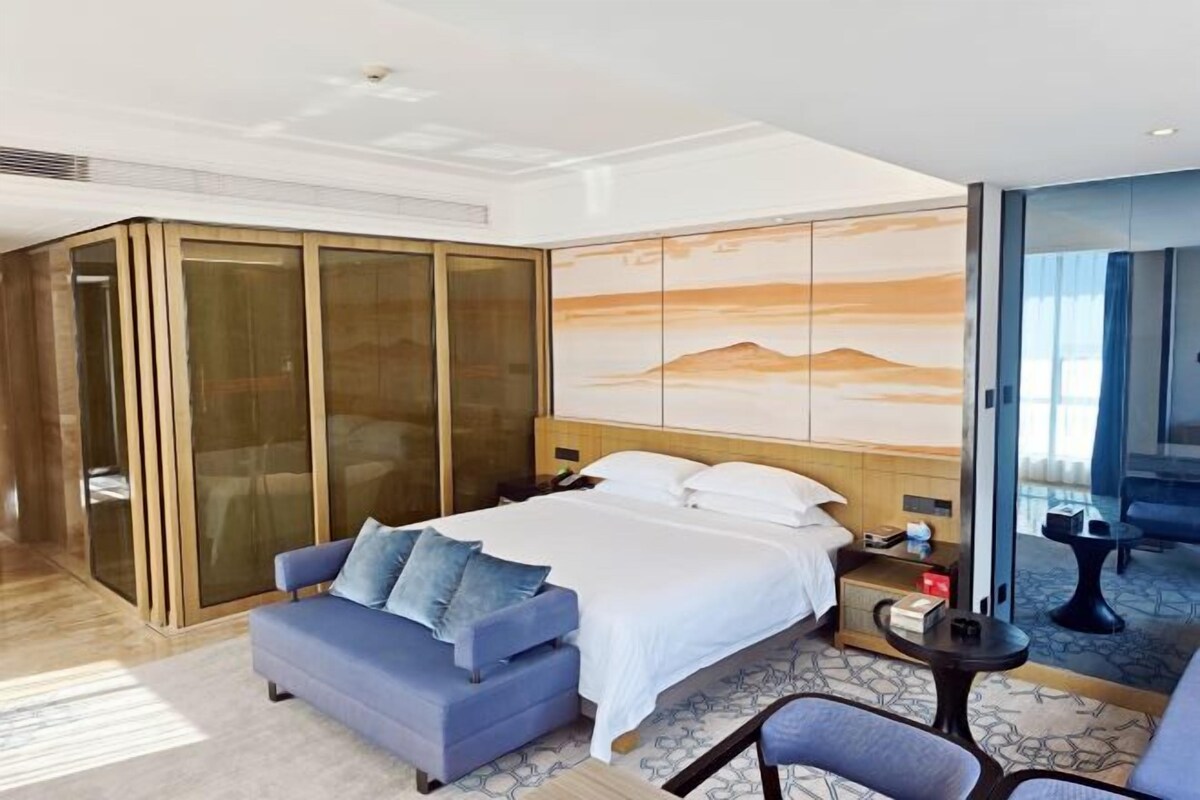 Ein Hotelzimmer mit einem Bett, einer Couch, einem kleinen Tisch und einer Glastrennwand.