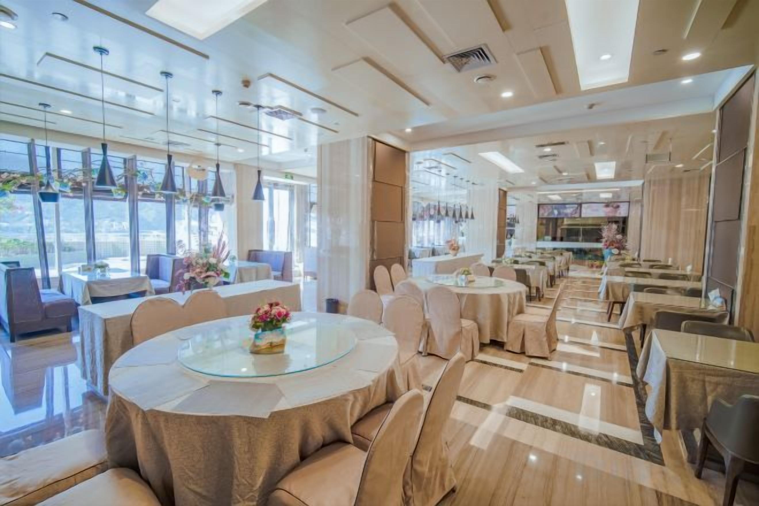A spacious dining area with round tables and chairs, large windows, and a modern interior design.