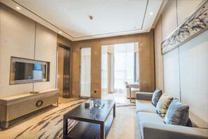 Ein modernes Wohnzimmer mit Flachbildfernseher, Couchtisch aus Holz, einer Couch und einem großen Fenster.