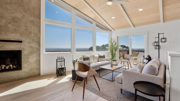 A spacious living room with a fireplace, large windows, and a ceiling fan.
