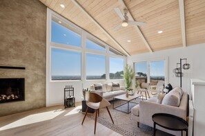A spacious living room with a fireplace, large windows, and a ceiling fan. - 7-acre, Sweeping Views, Hot Tub, Volley Ball, Close to Downtown! (Paso Robles)