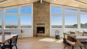 A spacious room with a high ceiling, large windows, a fireplace, and a dining area.