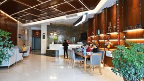 A modern hotel lobby with a reception desk, seating area, and a large potted plant. - Mingzhu Hotel (Qingchuan)