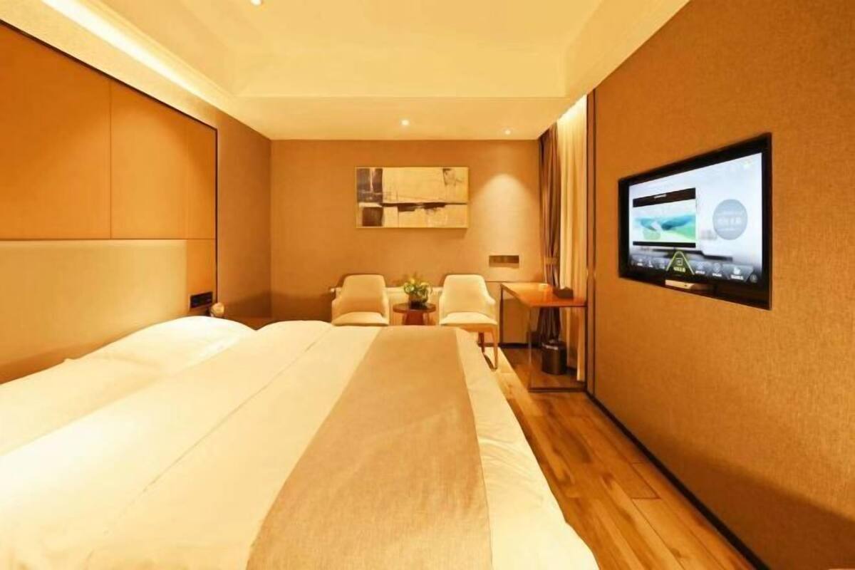 A hotel room with a large bed, a desk with a computer, a TV on the wall, and a seating area with chairs.