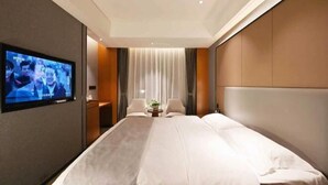 A hotel room with a bed, a TV mounted on the wall, a small table with a plant, and a window with curtains. - Mingzhu Hotel (Qingchuan)