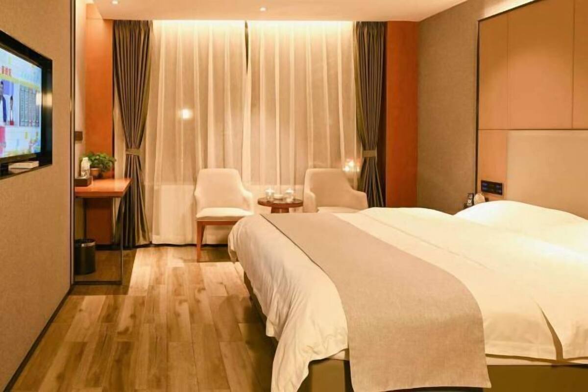 A hotel room with a large bed, two chairs, a small table, a TV, and curtains.