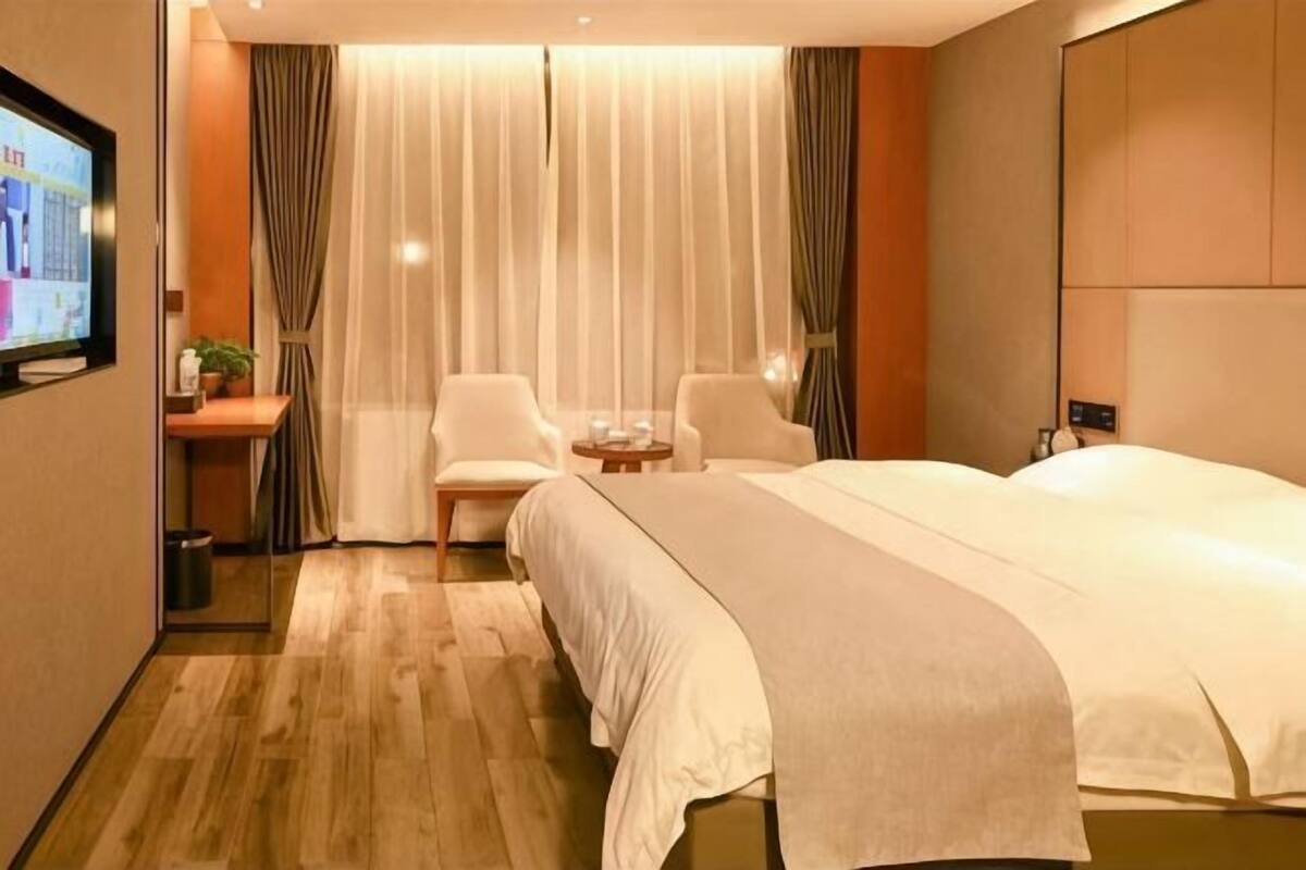 A hotel room with a bed, two chairs, a small table, a TV, and curtains.