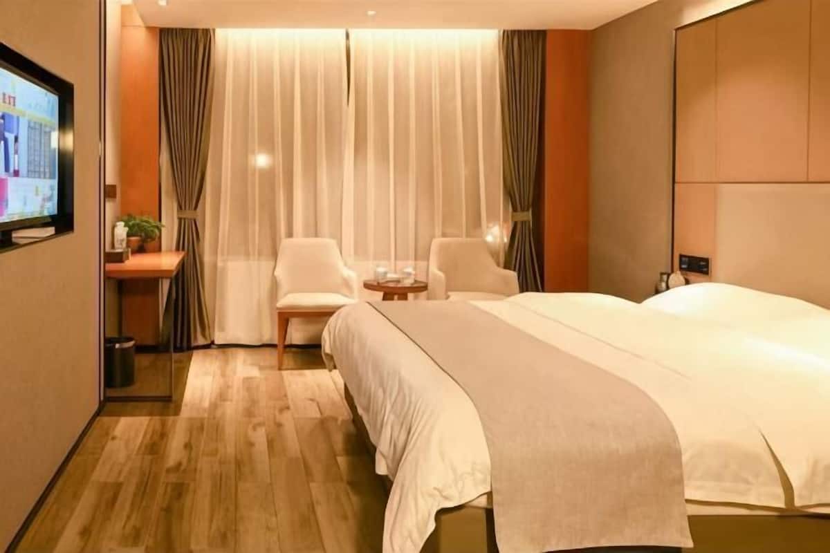 A hotel room with a bed, two chairs, a small table, a TV, and a window with curtains.