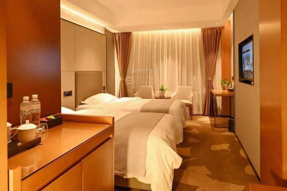 A hotel room with two beds, a desk, a chair, a small table, and a large window with curtains.