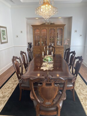 A formal dining room with a large wooden table, ornate chairs, a chandelier, and a wooden cabinet with glass doors.