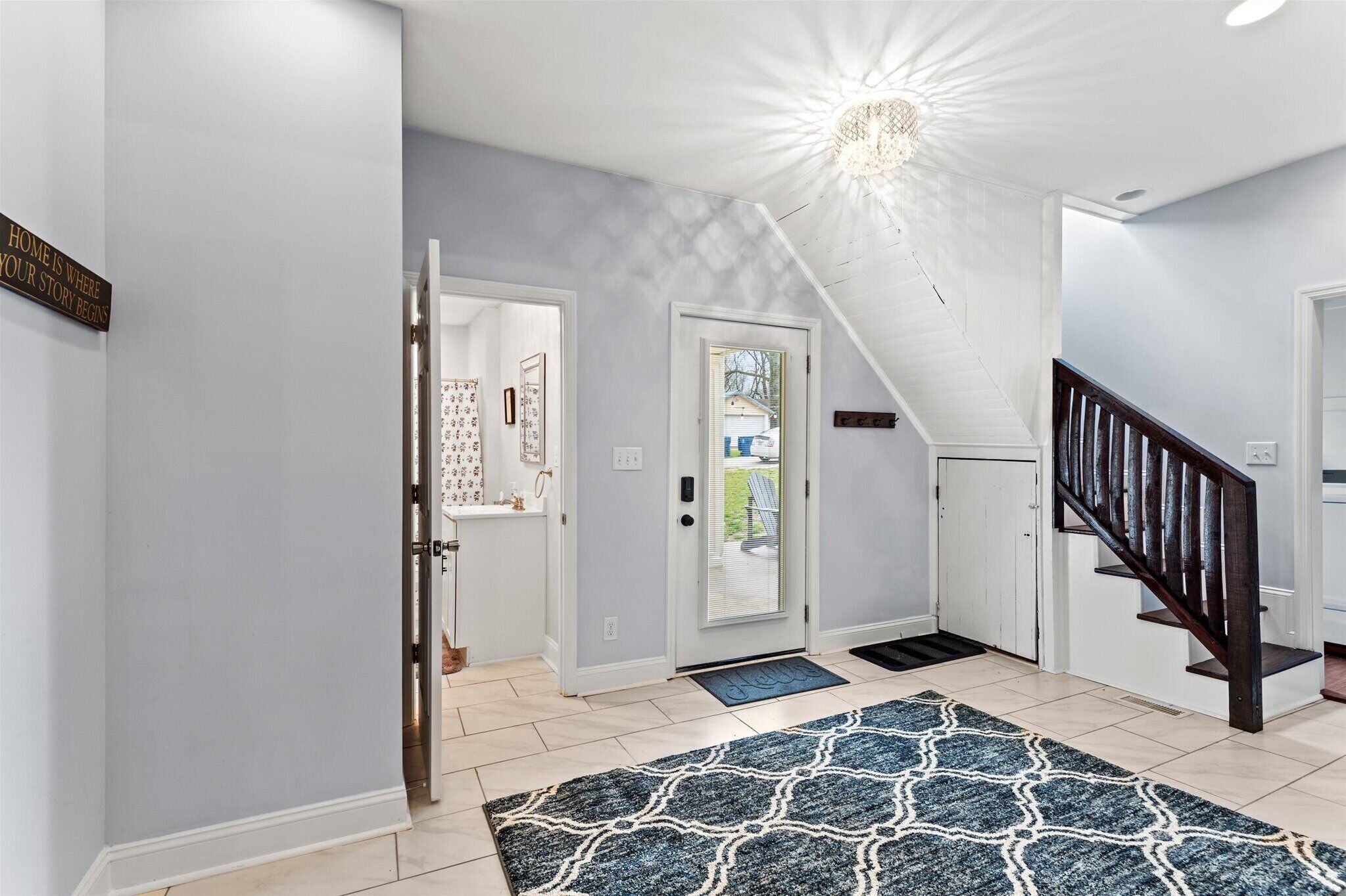 A hallway with a patterned rug, a staircase, and a door leading outside.