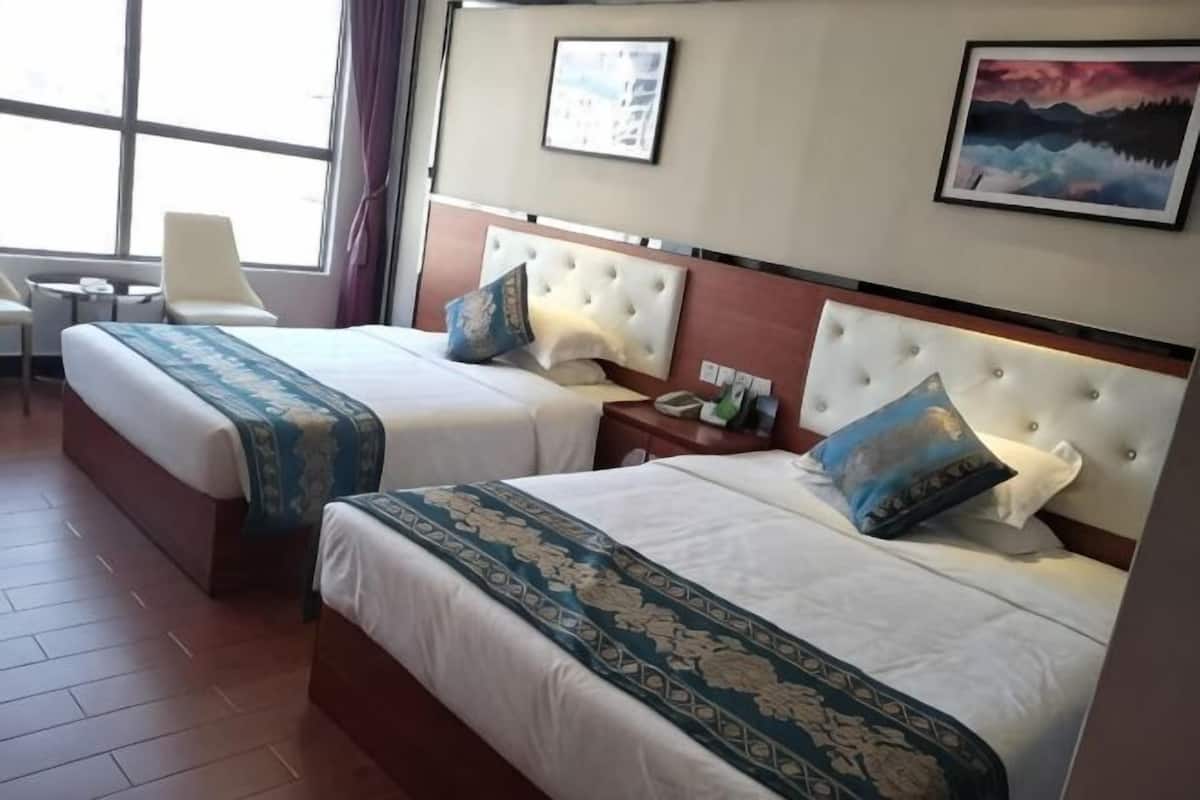 A hotel room with two beds, a chair, a desk, and a window with curtains.
